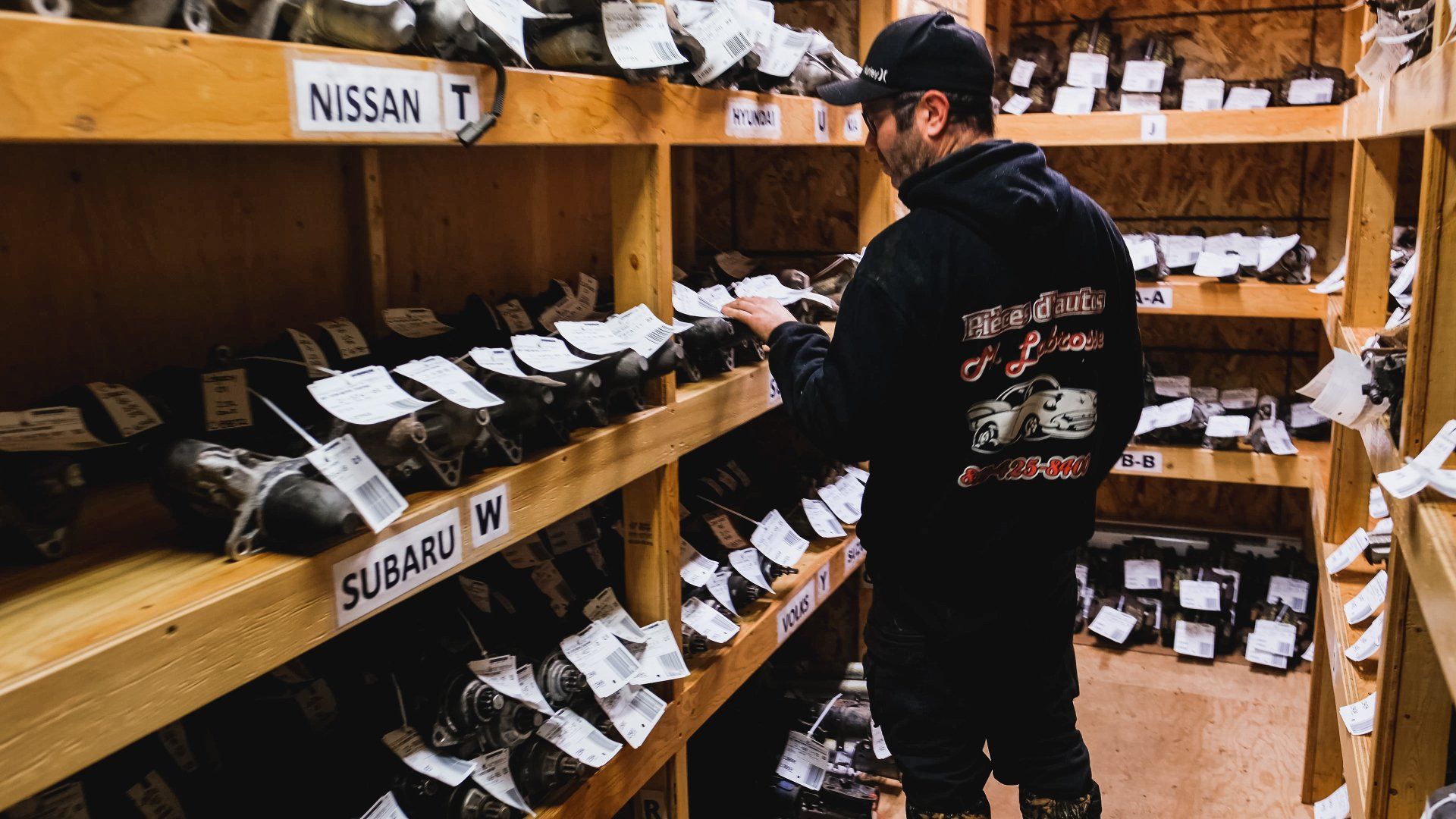 Une personne examine des pièces automobiles sur des étagères étiquetées Nissan et Subaru.