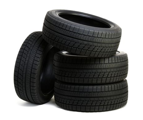 Quatre pneus de voiture noirs empilés, l'un d'eux appuyé contre la pile. Fond blanc.