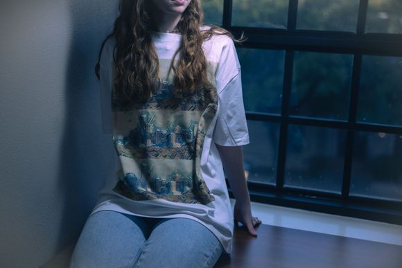 girl sitting on a table in a spotlight with a drop-shoulder t-shirt that displays the austin skyline three times