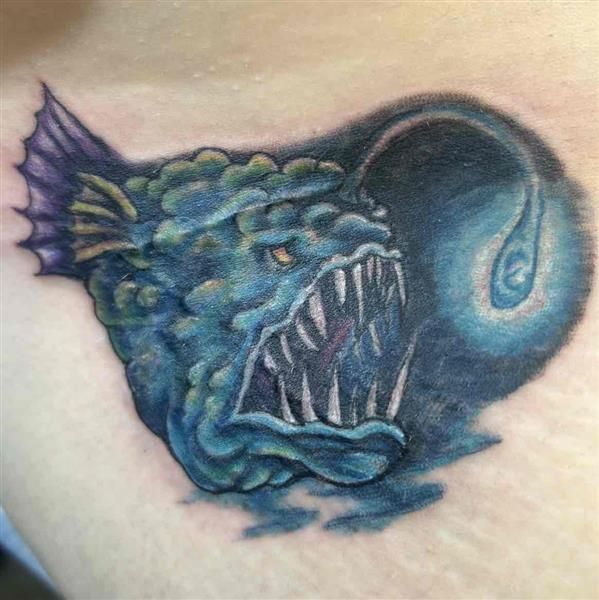Blue-green monstrous fish tattoo with sharp teeth and a dark swirling background