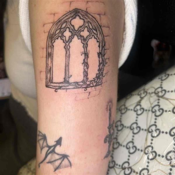 Close-up of a forearm tattoo featuring a gothic arched window outline in black ink.