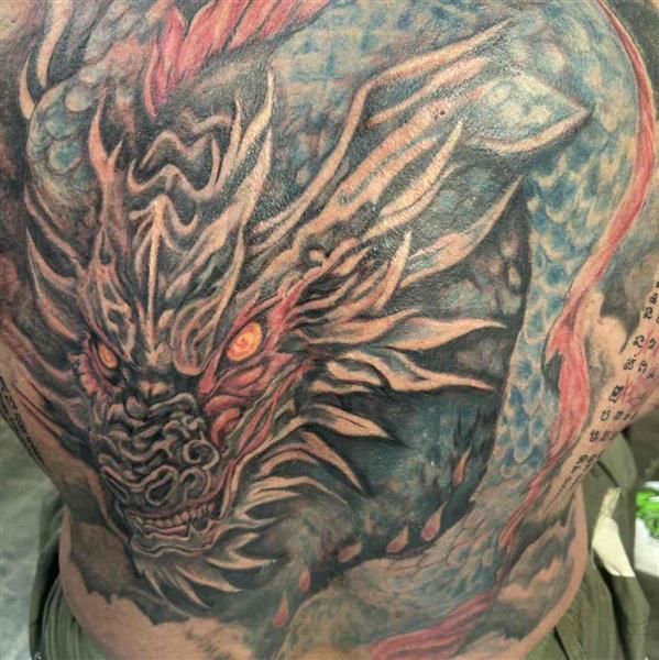 Close-up of a colorful dragon tattoo with fiery orange accents on a person’s back