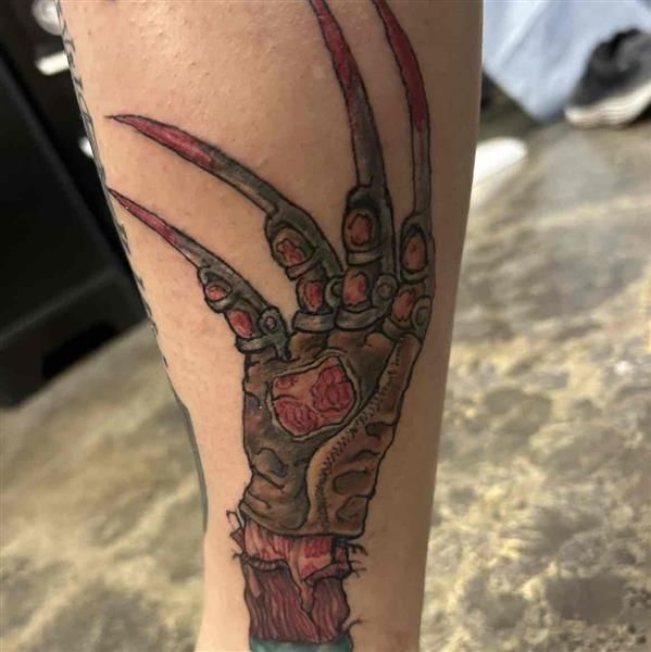 Tattoo of a skeletal hand with long claws in red, black, and gray ink on a calf