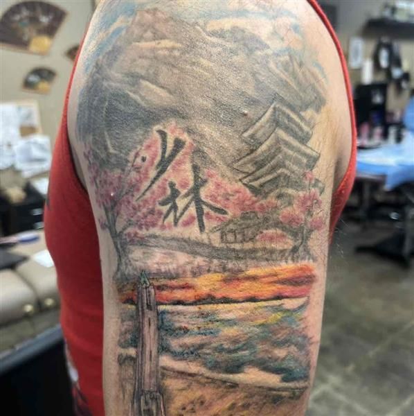 Close-up of a tattooed upper arm showing a colorful landscape and red Chinese characters.