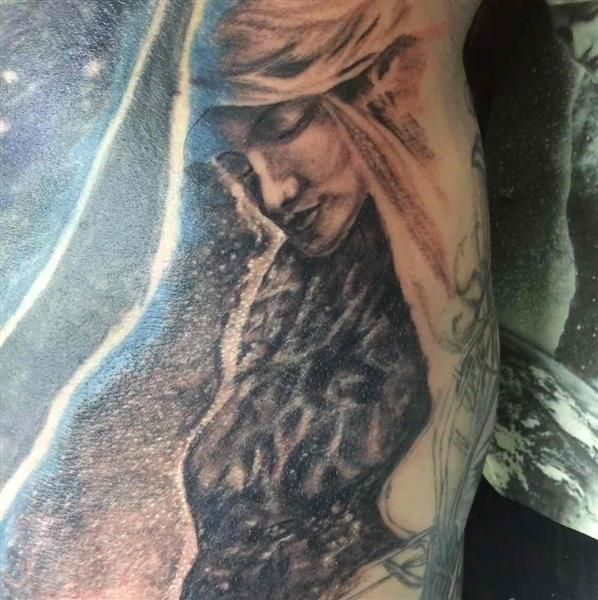 Close-up of a black-and-gray tattoo showing a woman with long hair and a soft, downward gaze.