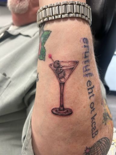 Forearm tattoo of a martini glass with an olive, next to vertical French text.