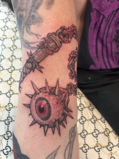 Close-up of an arm tattoo showing a red eye with spiked rays and dark chain-like links around it