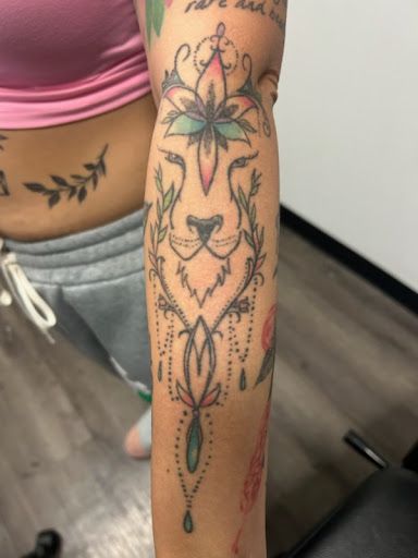 Forearm with colorful floral and geometric tattoo design, showing a stylized face motif
