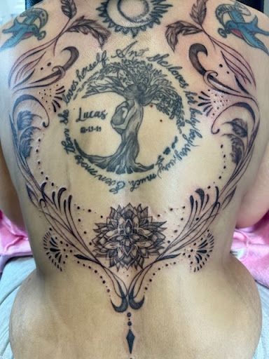 Back tattoo with tree of life, floral swirls, and decorative mandala designs on a bare back
