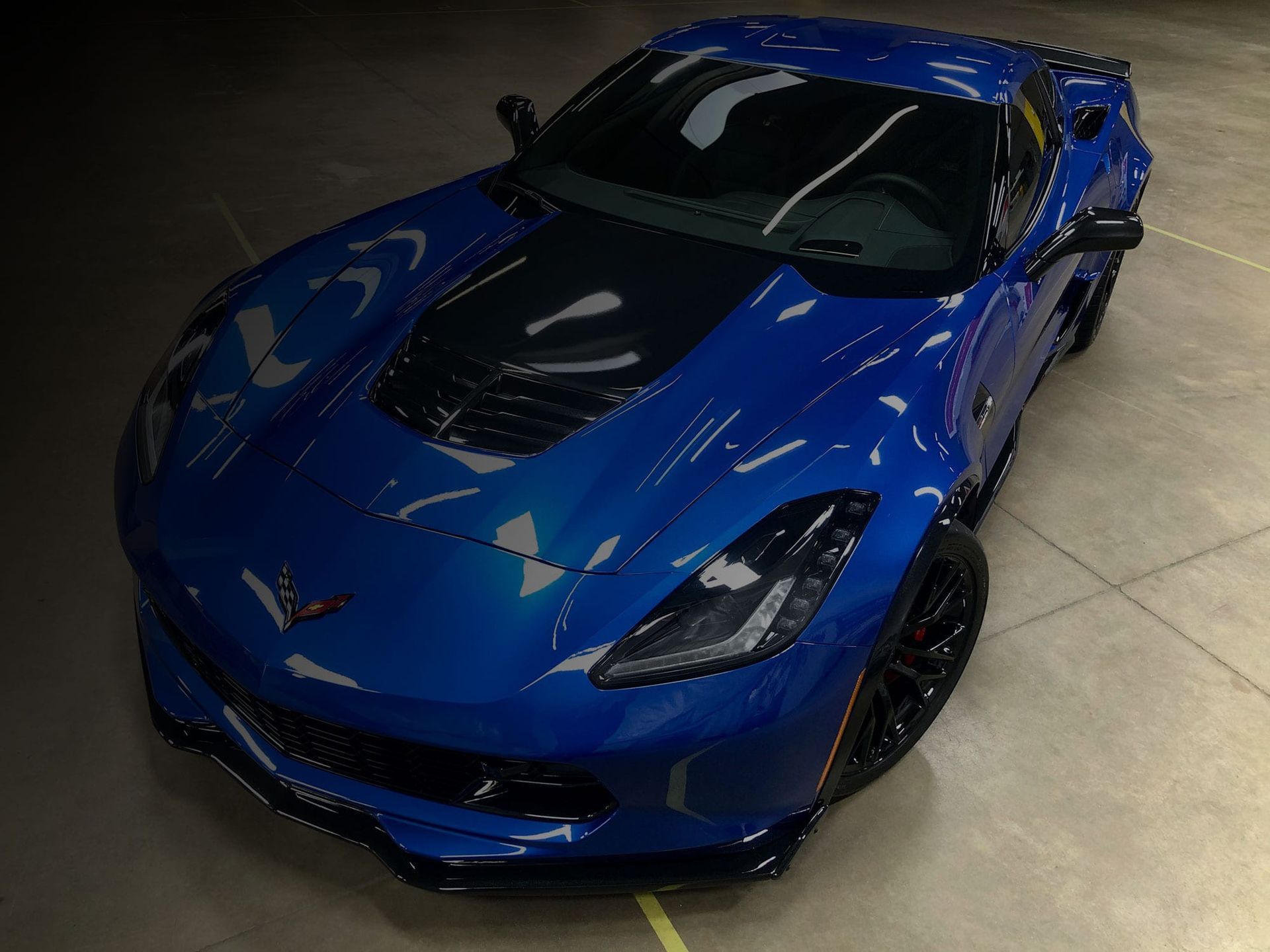 High-angle shot of a blue Chevrolet Corvette parked on a light concrete floor.
