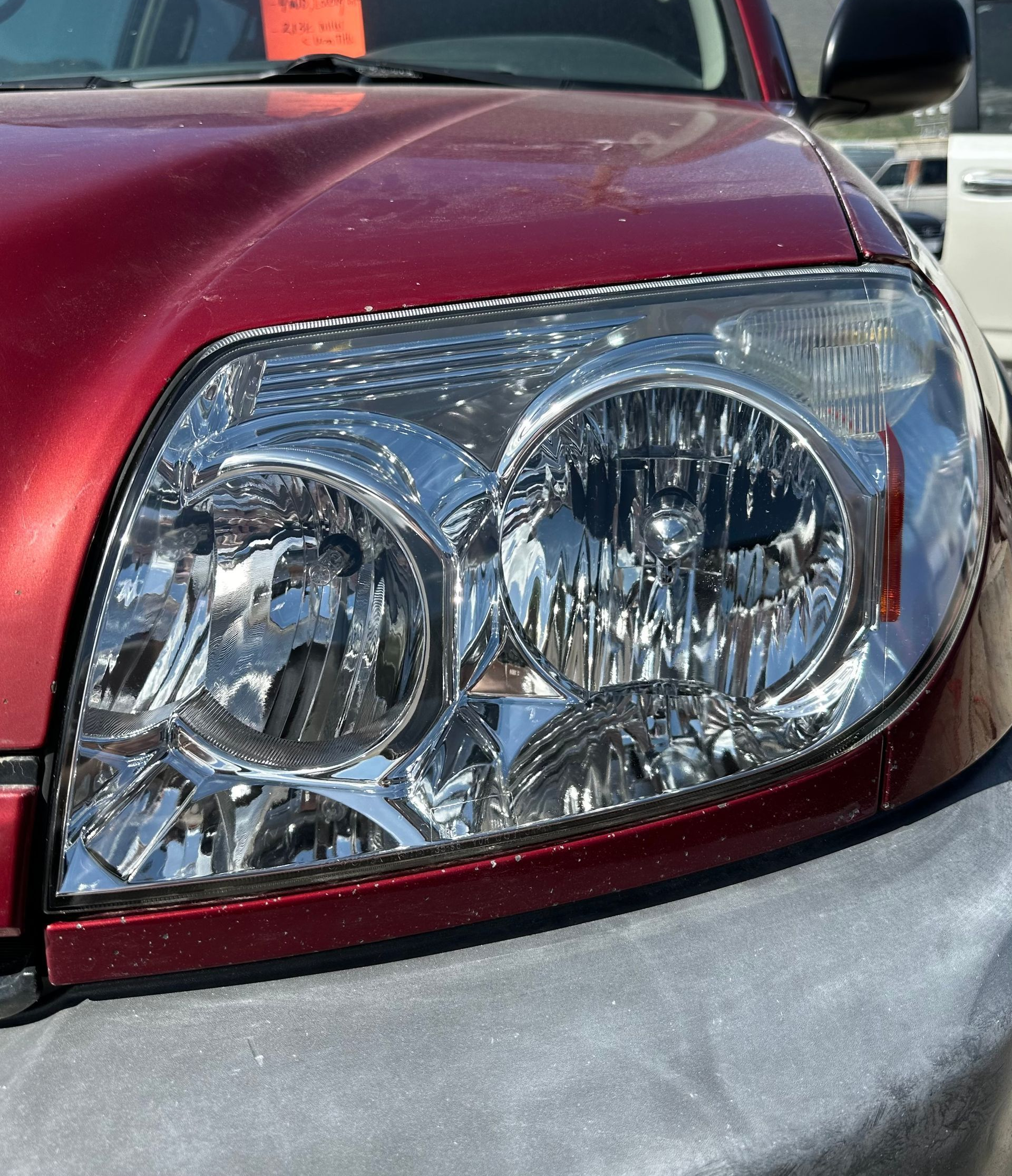 A close-up of a red vehicle's headlight with a red price tag hanging from the rearview mirror.