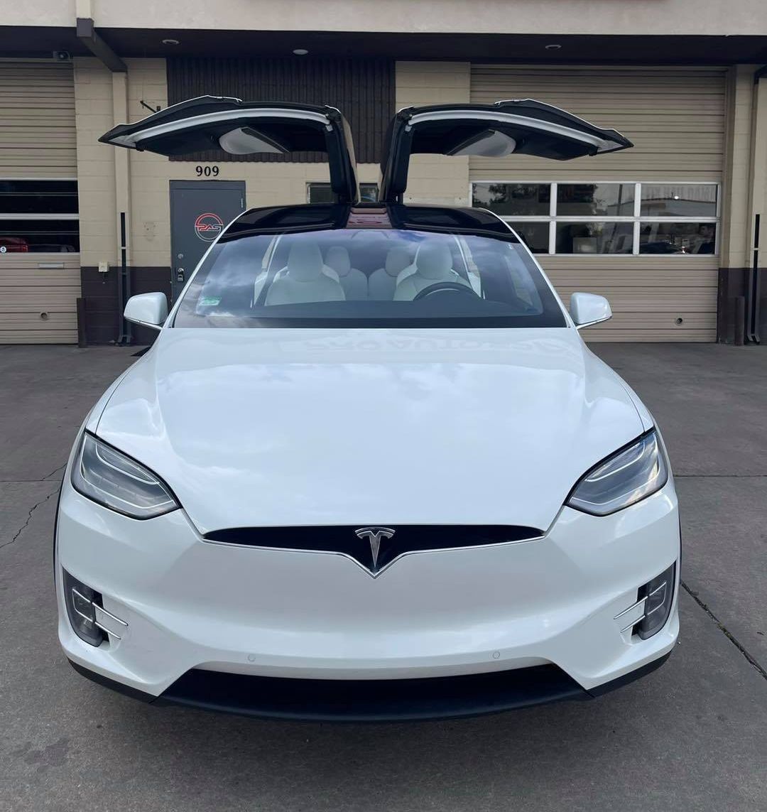 A white Tesla Model X parked in front of a building with its falcon-wing doors open.