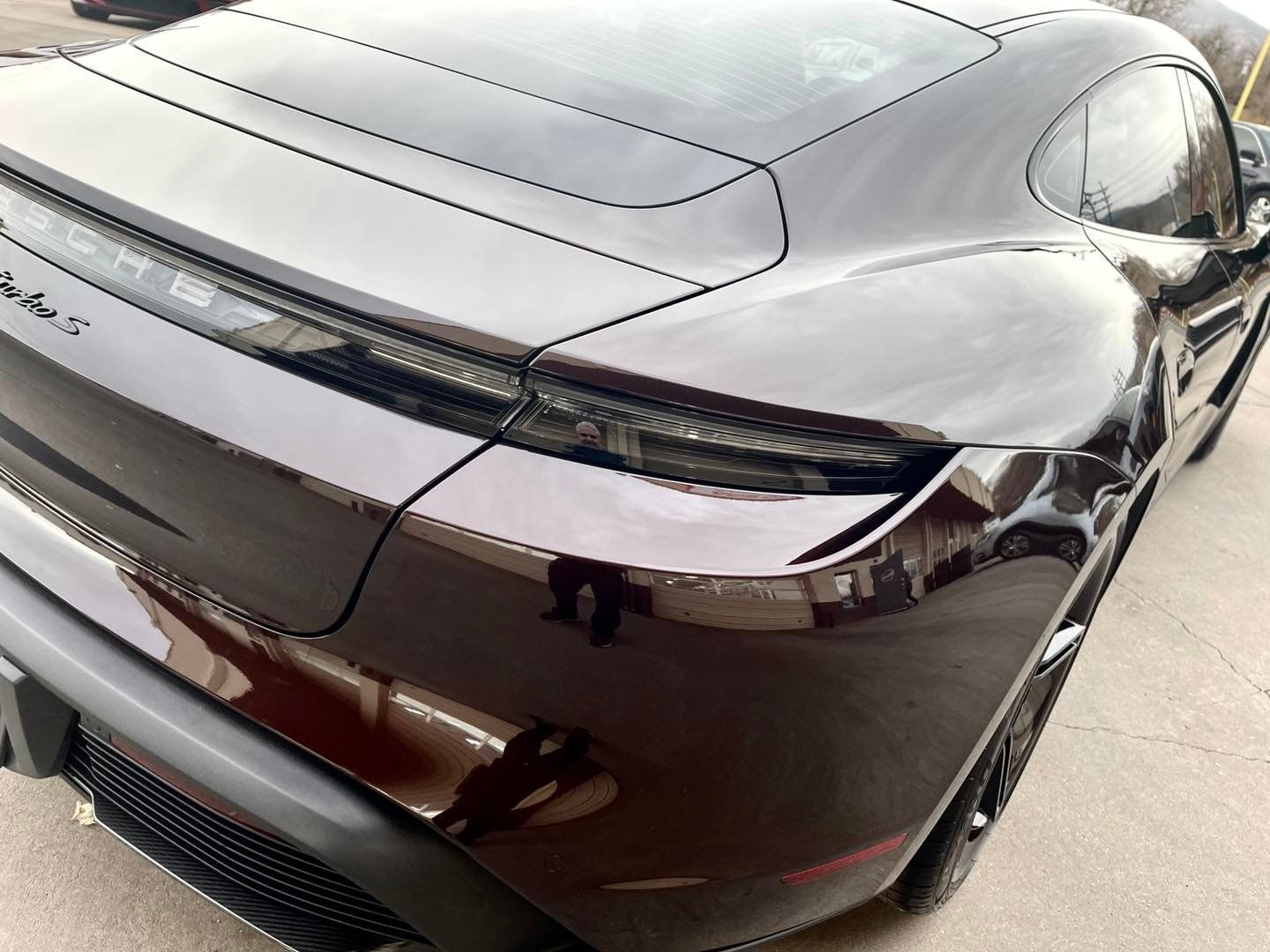 The rear view of a dark metallic Porsche Taycan, showcasing its sleek taillight design and curved bodywork.