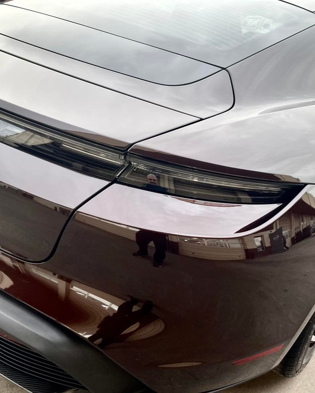 A technician applies a clear protective paint film to the front bumper and headlight of a gray car.