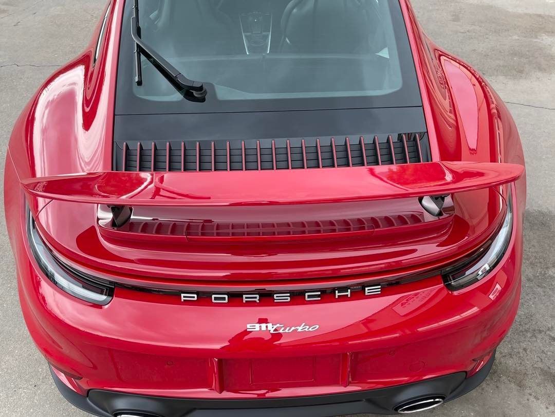 A high-angle view of the rear of a bright red Porsche 911, showing its spoiler, iconic taillight bar, and dual exhausts.