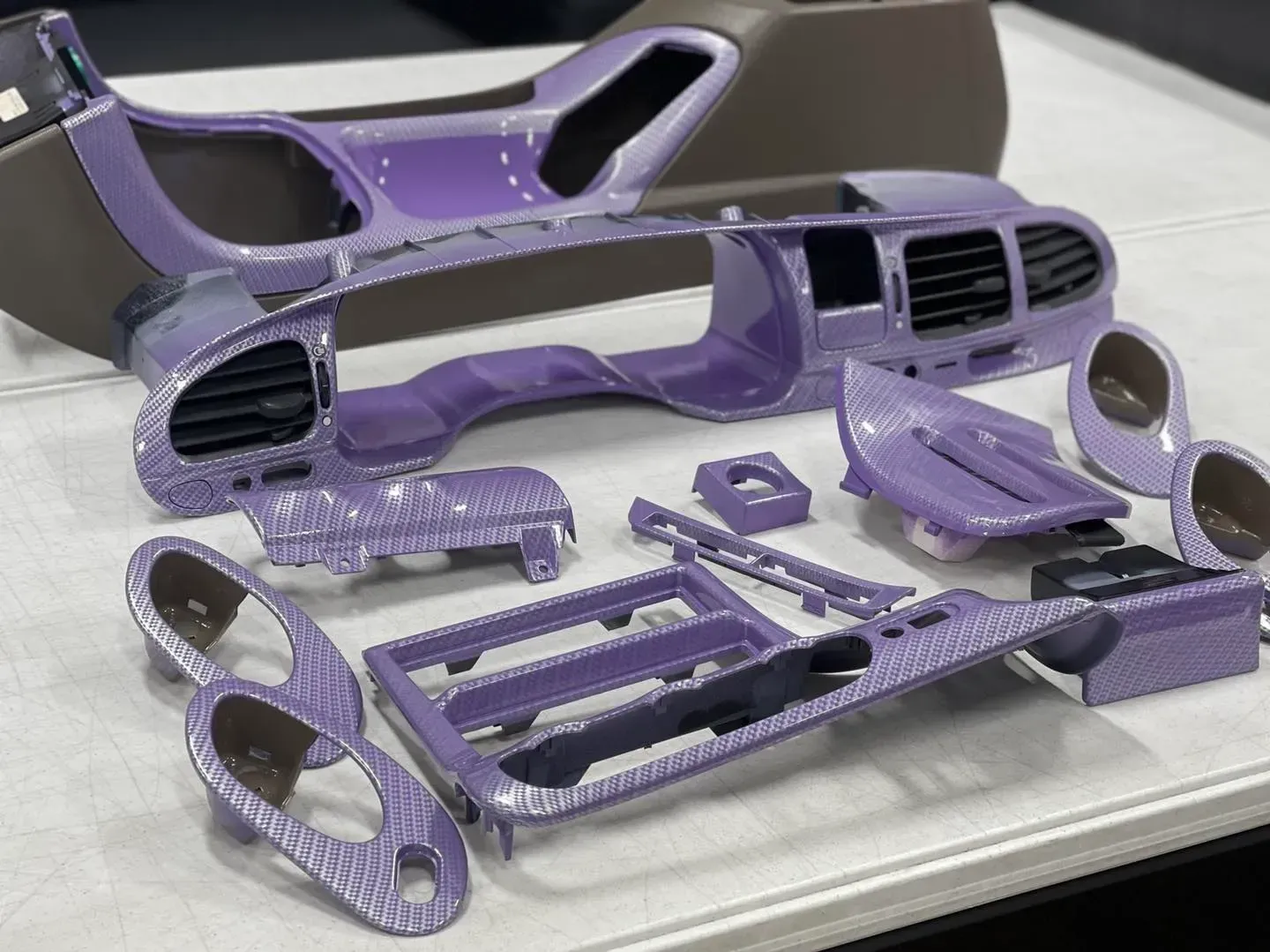 Various car interior plastic trim pieces, customized with a light purple snake-skin pattern, arranged on a white table.
