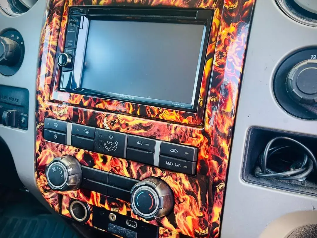 Vehicle center console with a flame-patterned trim surrounding a touchscreen infotainment system and climate controls.