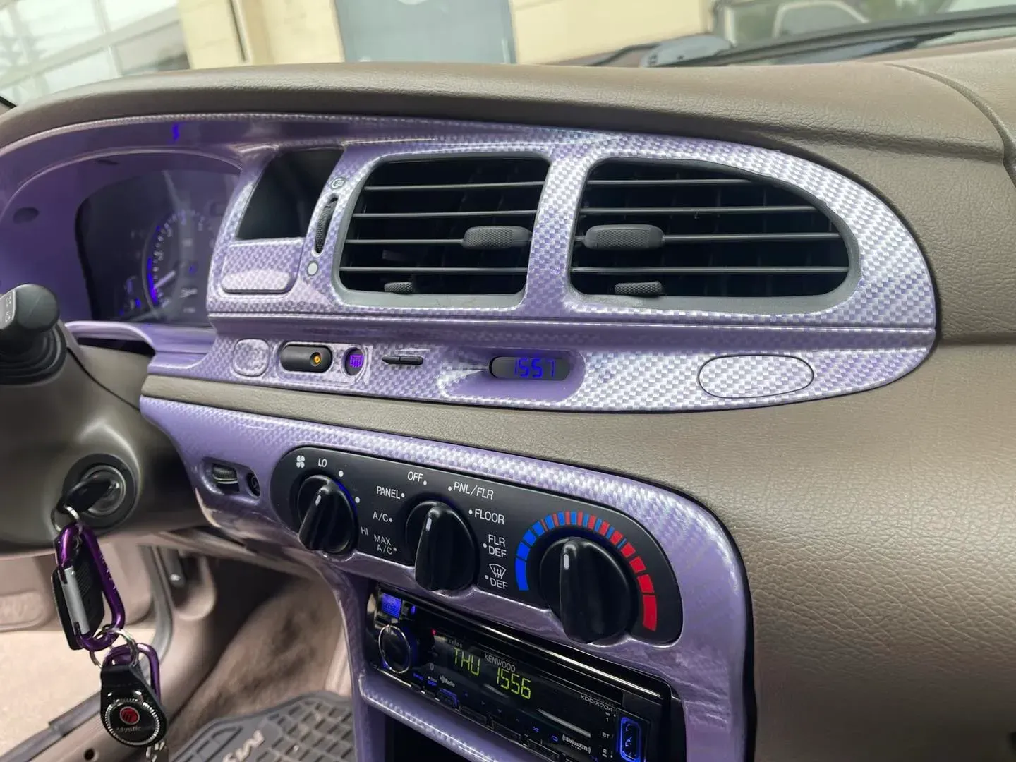 Car interior showing a dashboard with purple carbon fiber-style trim, air vents, climate controls, and a radio.
