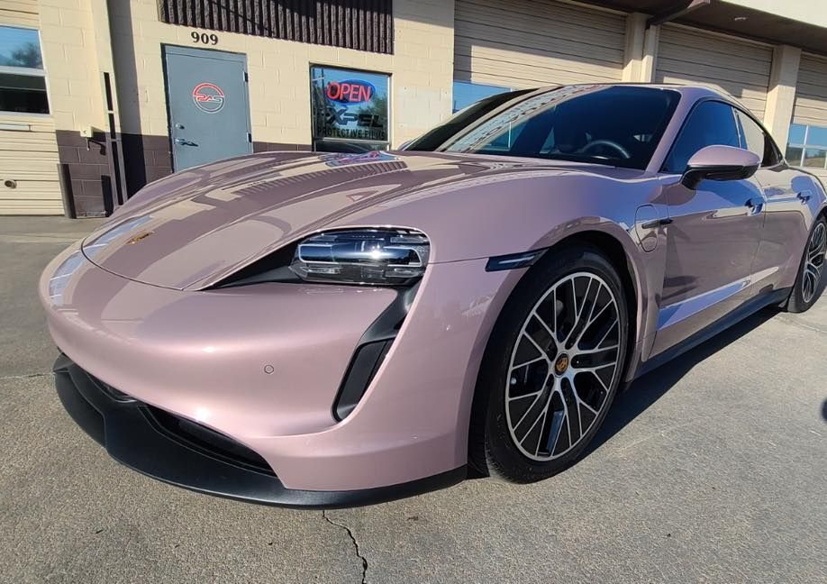 A light pink Porsche Taycan parked in front of a commercial building with an open door.