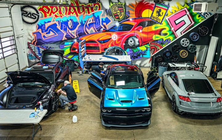 Cars in a garage with colorful graffiti art. Mechanics work on the vehicles.