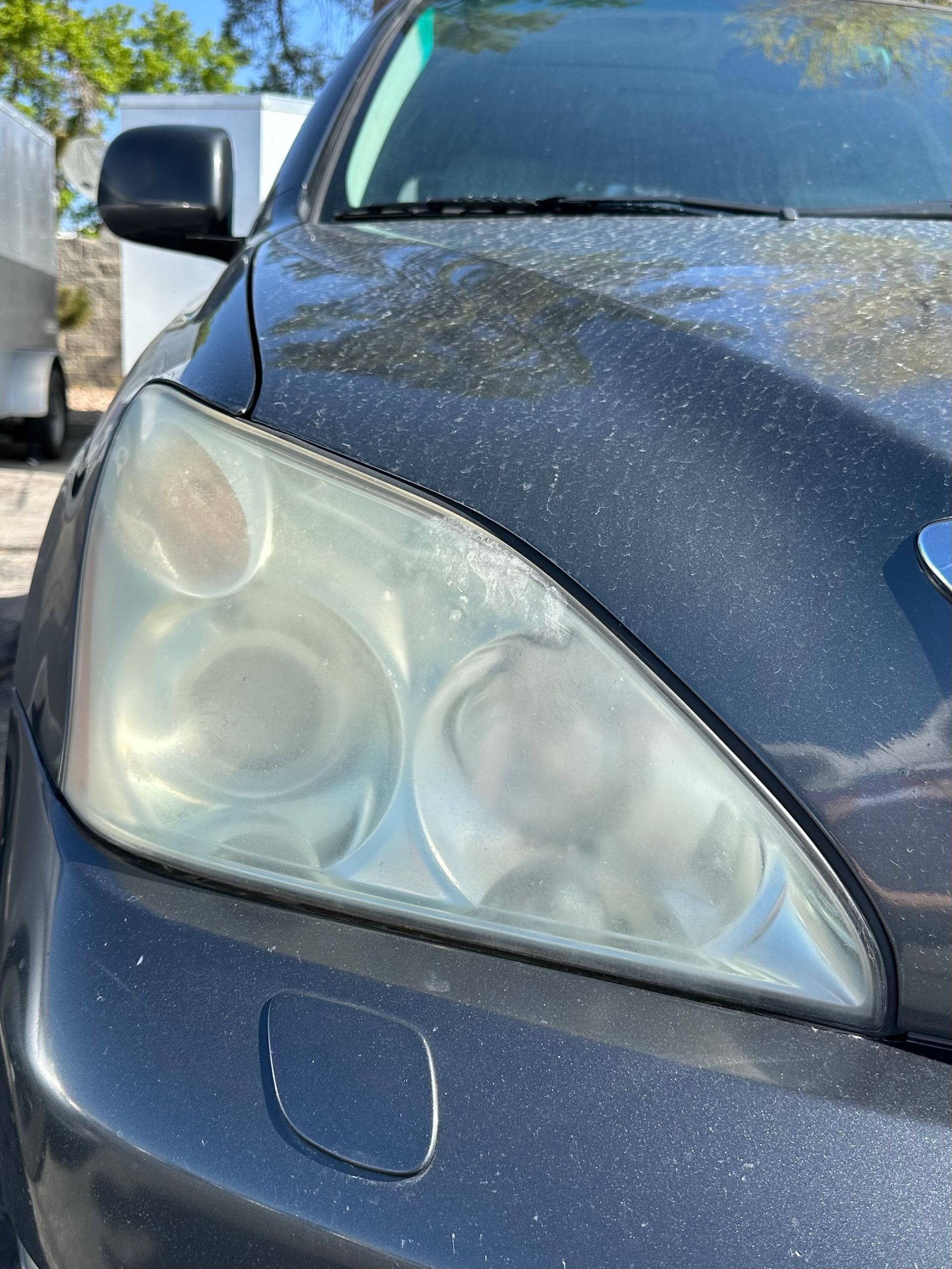 A close-up view of a dark, dusty car’s headlight, showing significant yellowing and oxidation on the plastic lens.