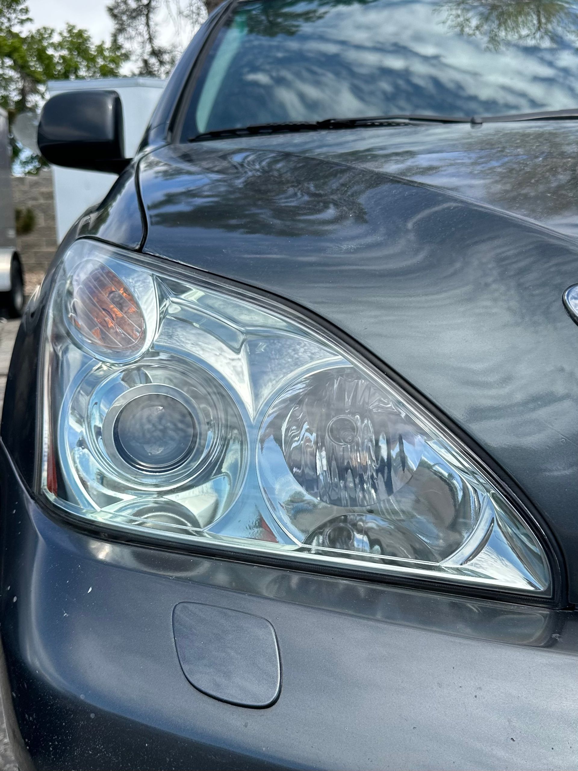 Close-up of a dark grey car's headlight assembly with a small, square panel on the front bumper below it.