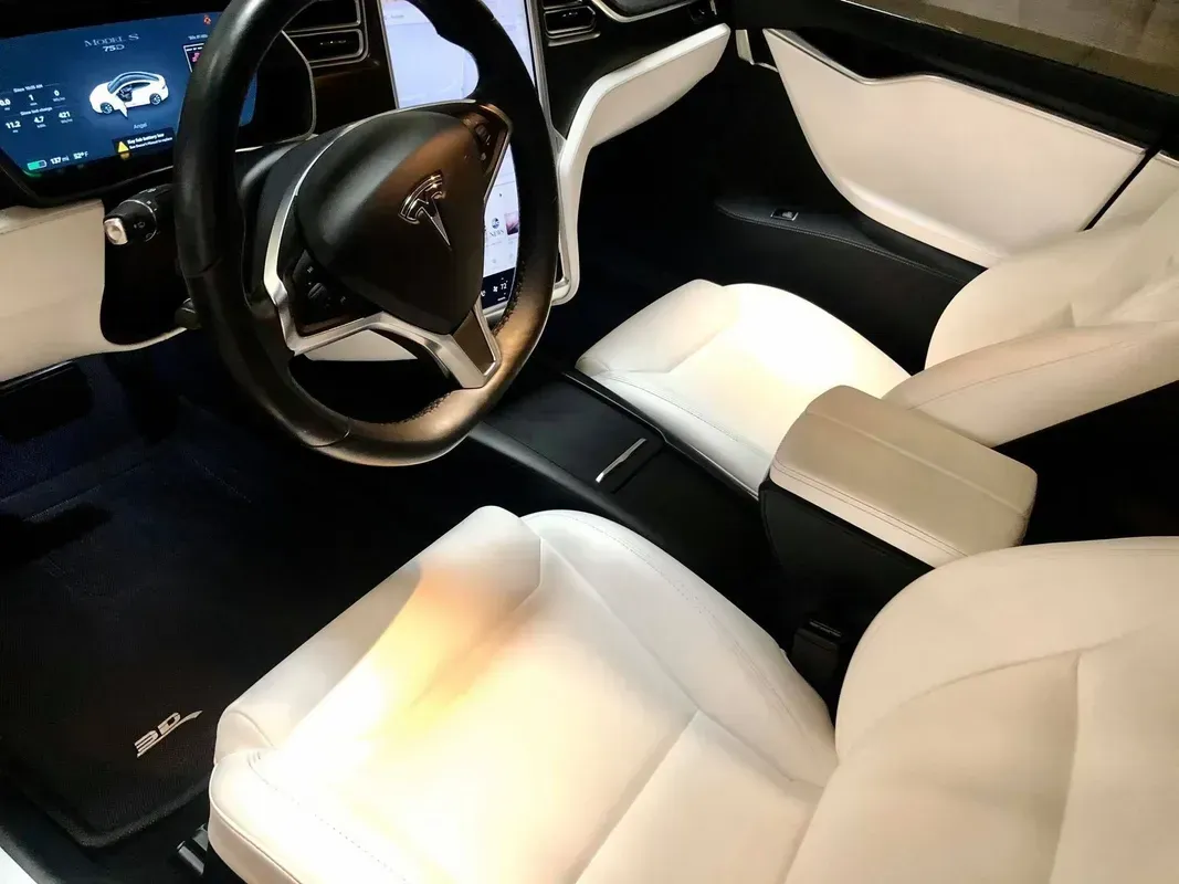Interior of a Tesla vehicle with a black steering wheel and white leather seats.