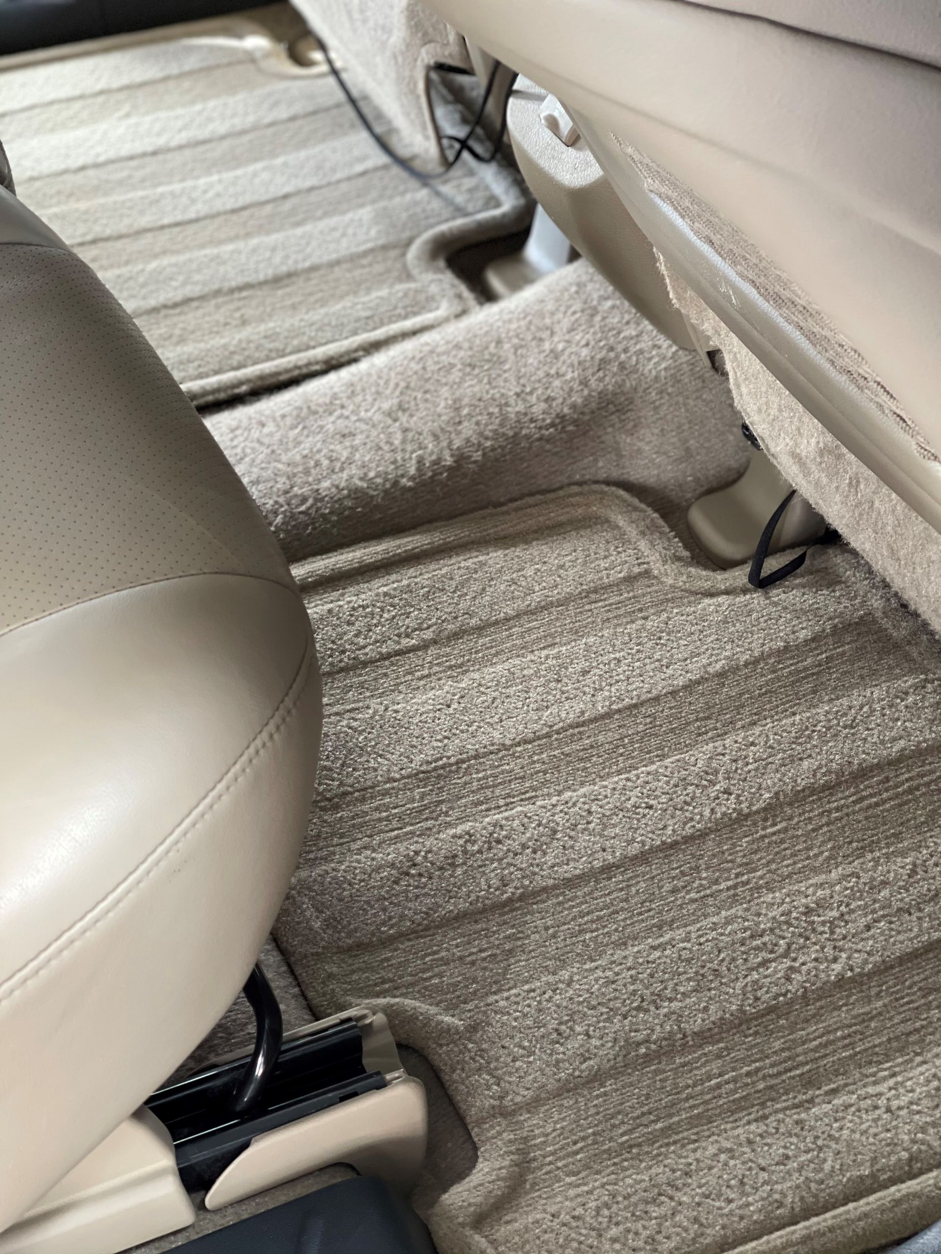 Tan-colored vehicle interior showing beige leather seating, fitted floor mats, and carpeted flooring.