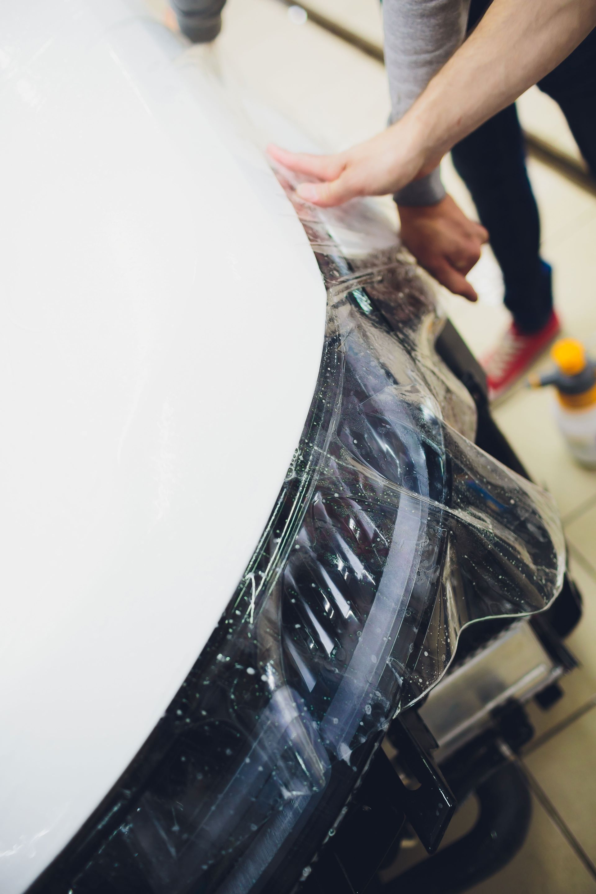 A person applies a clear protective film to the headlight of a white car.