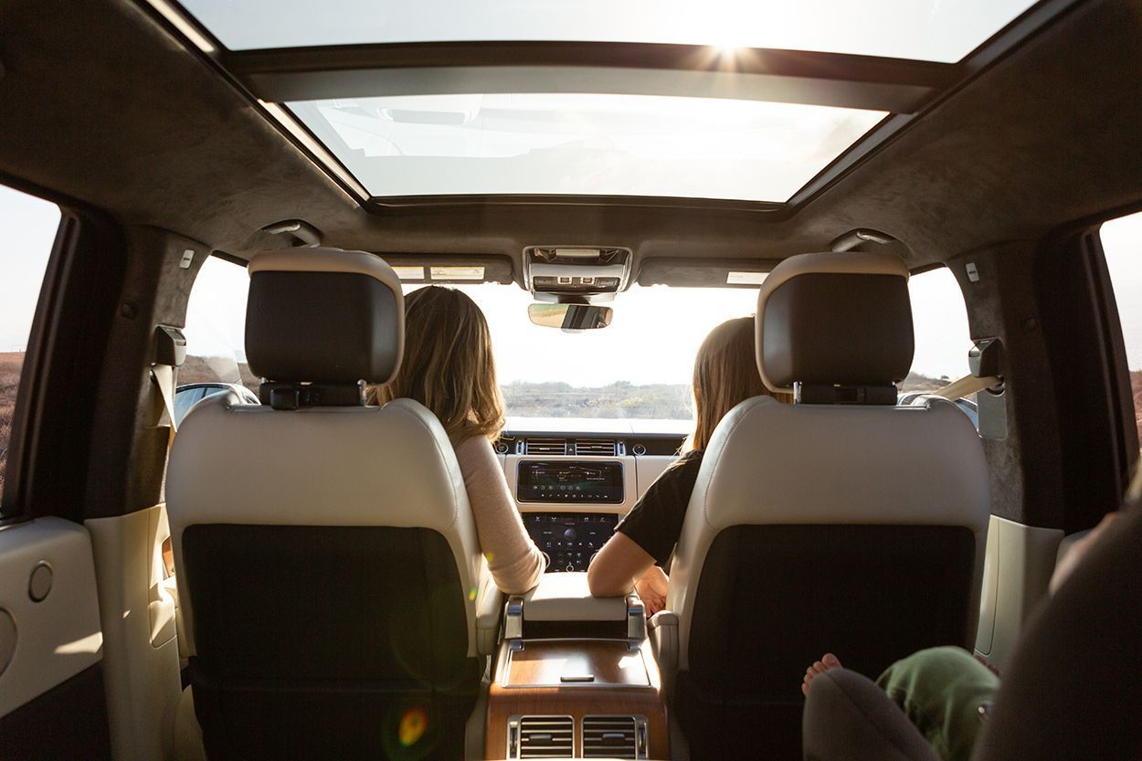 A rear-facing view from a vehicle's backseat showing two people sitting in the front seats under a large panoramic roof.