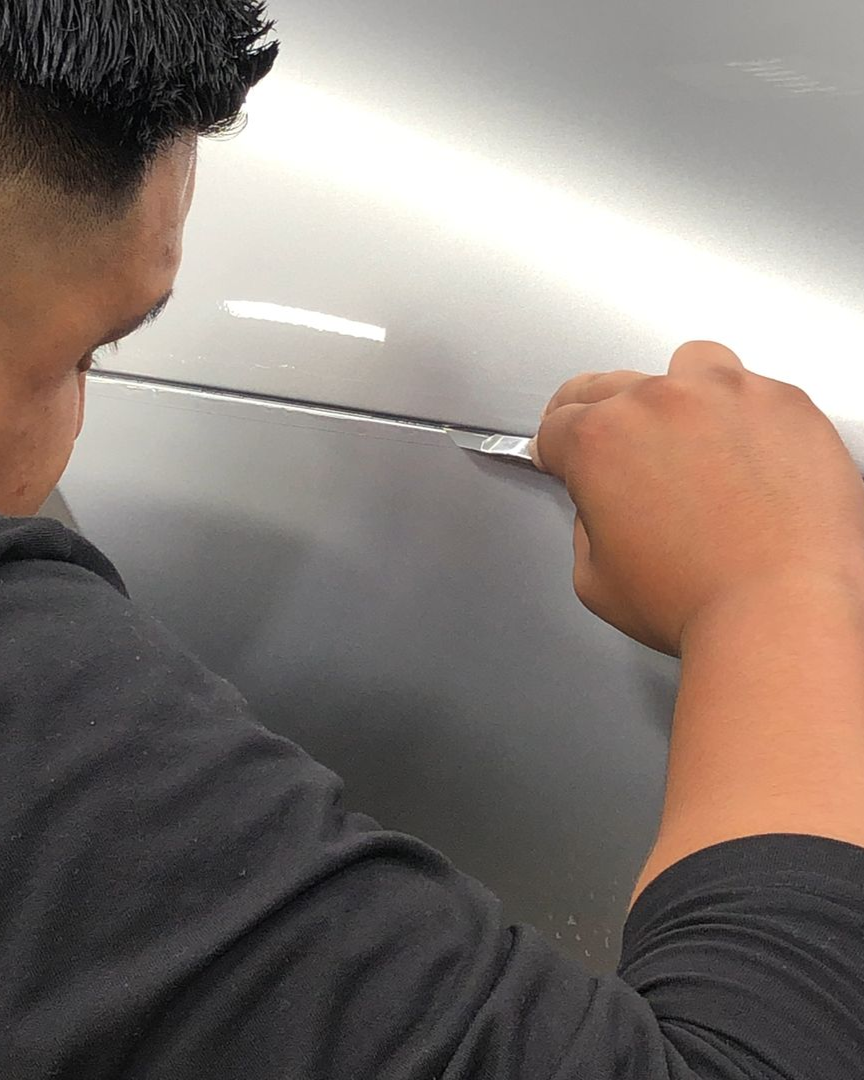 Person using a knife to cut a shiny metal surface close up