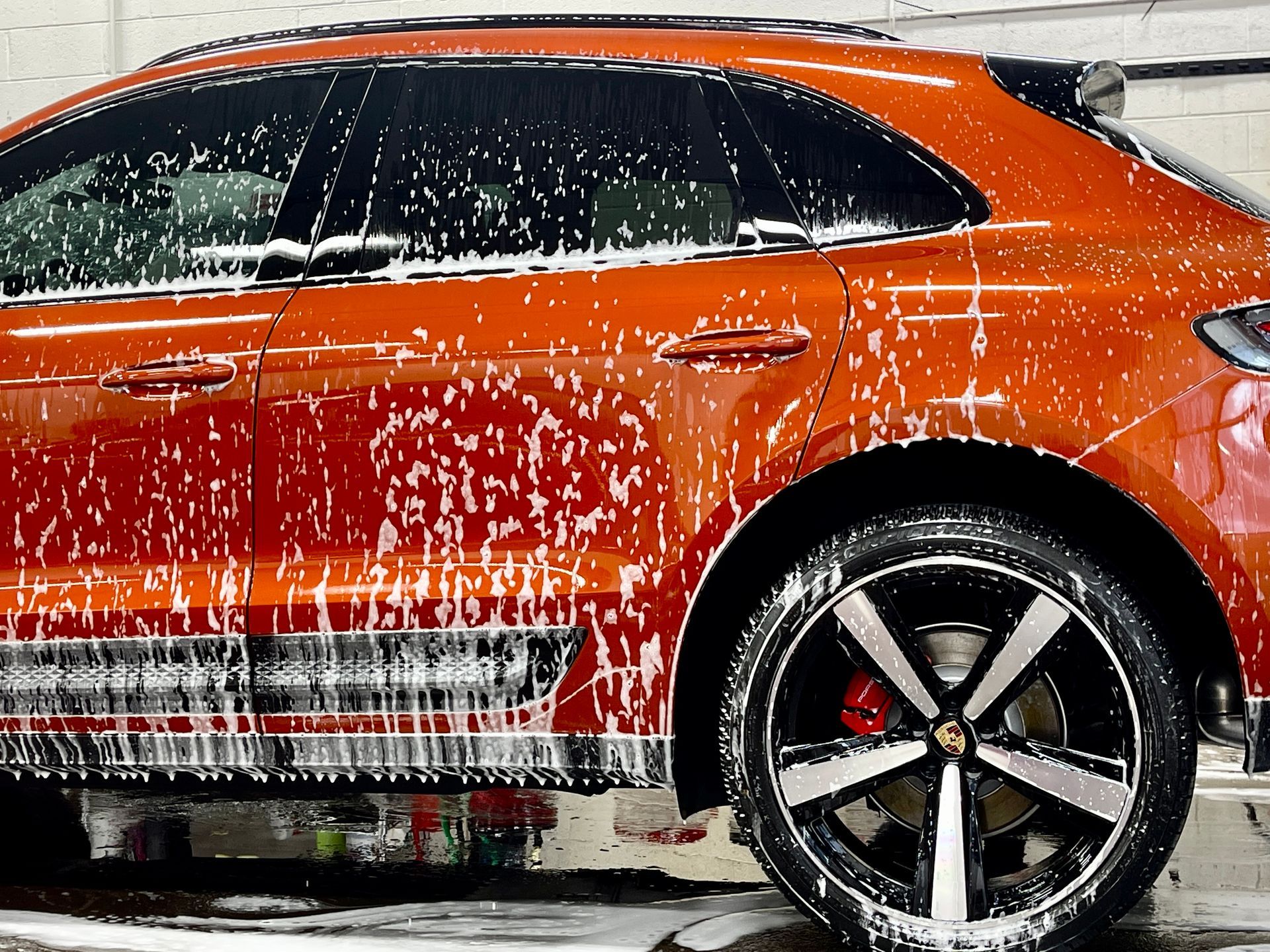 An orange car being washed with soap suds at a car wash.