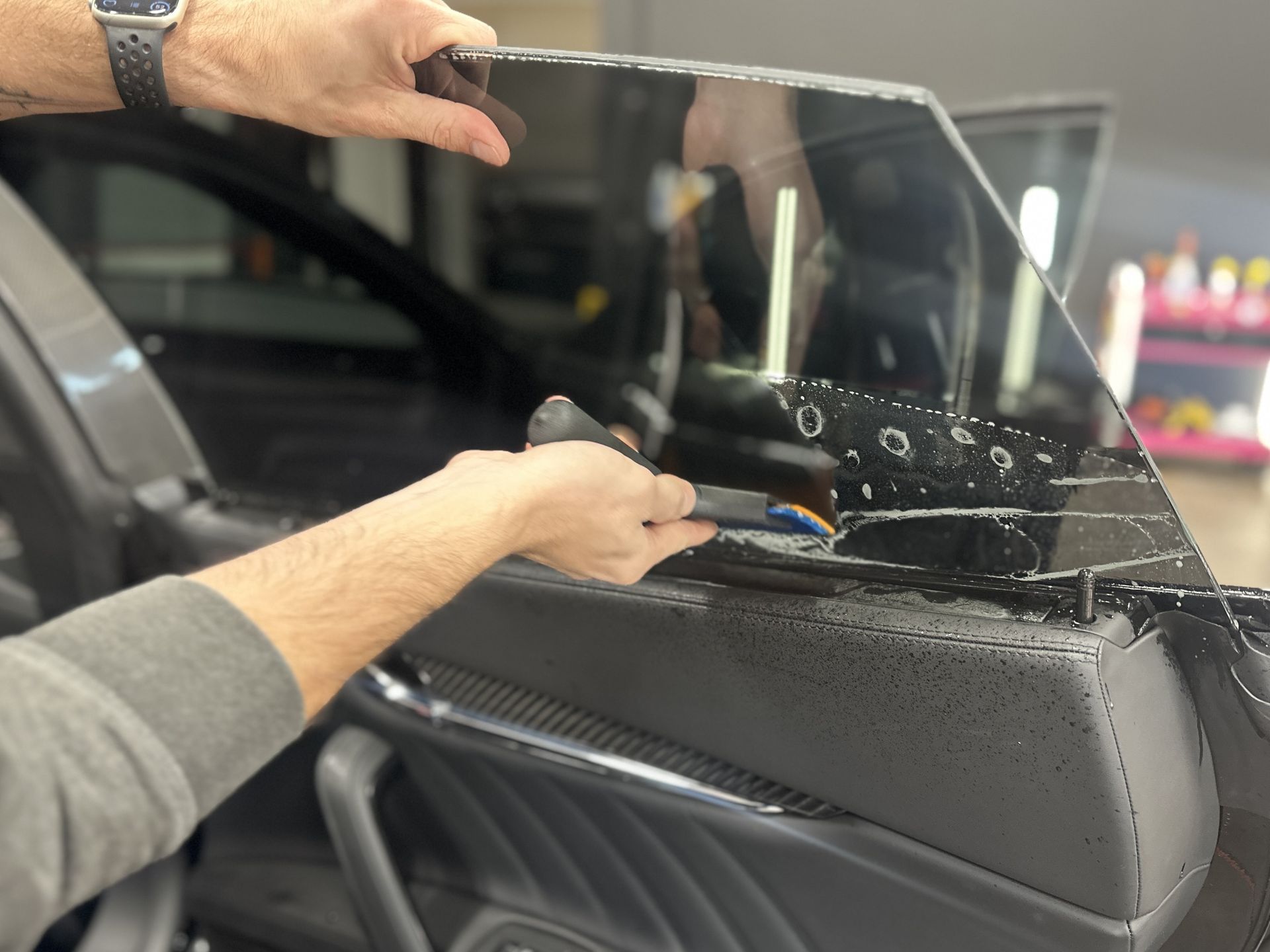 Hands installing a clear window film on a car side window.