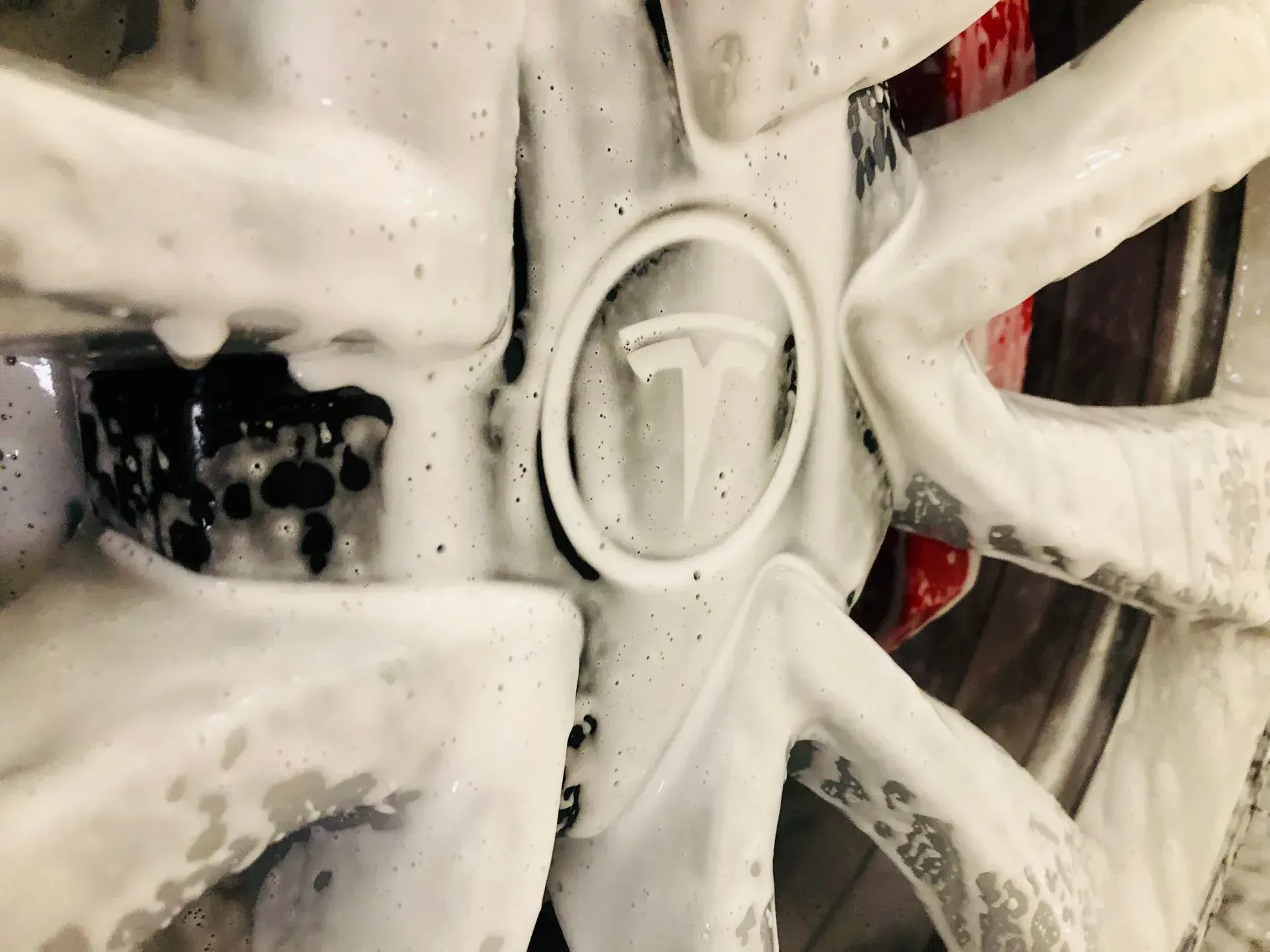 A Tesla vehicle wheel covered in thick, white soap suds during a car wash.