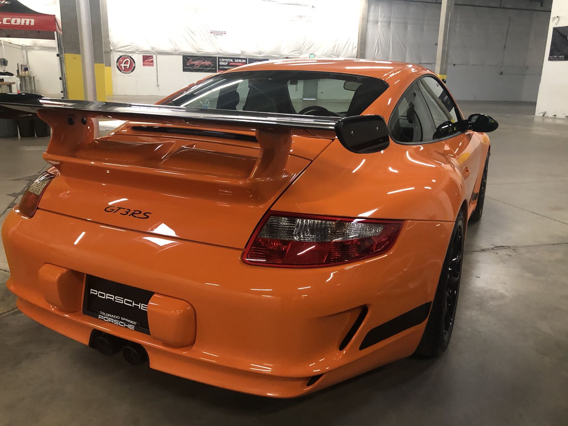 A bright orange Porsche 911 GT3 RS parked inside a warehouse with a large rear wing.