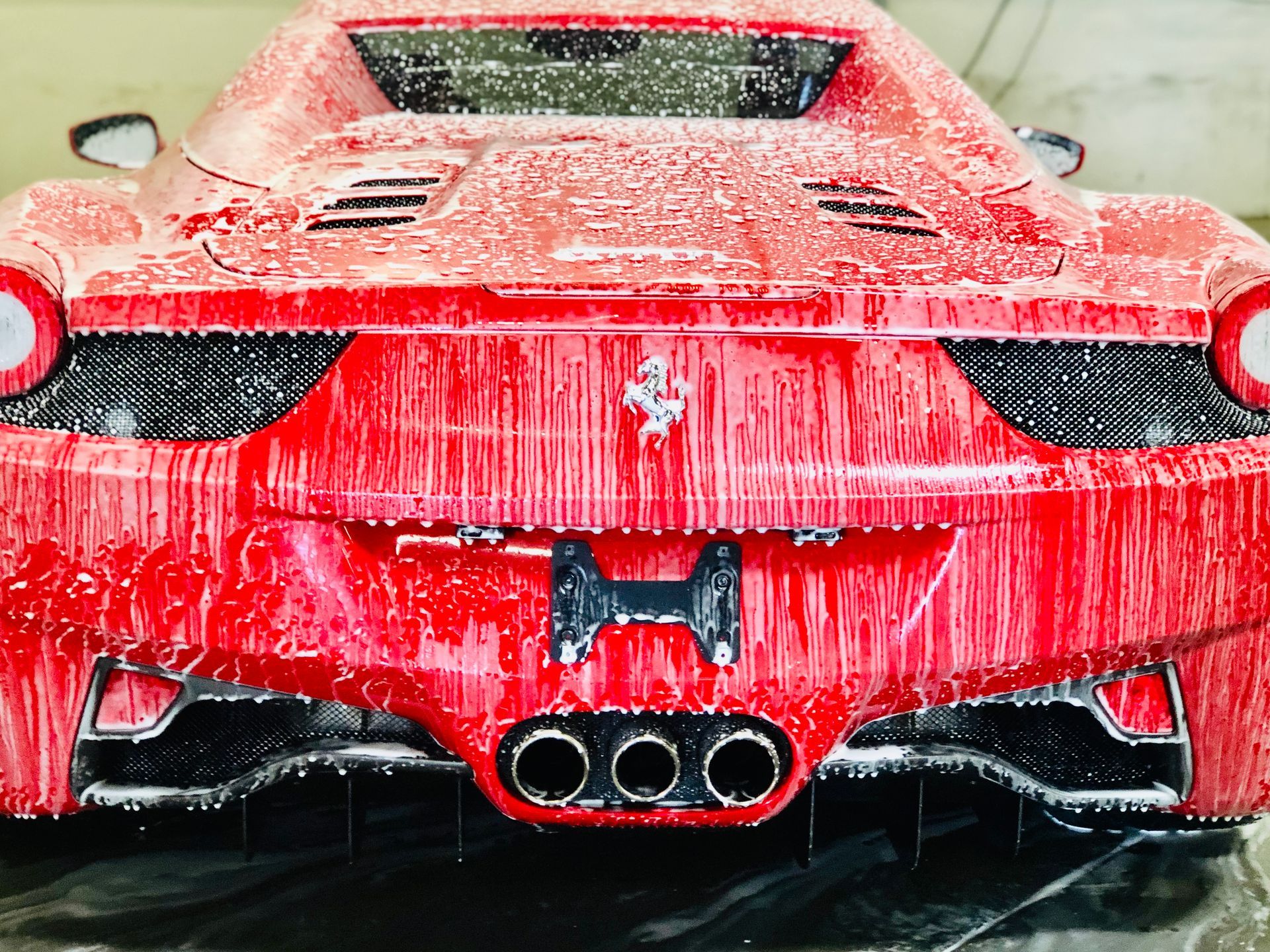 A bright red Ferrari covered in soapy foam while being washed.