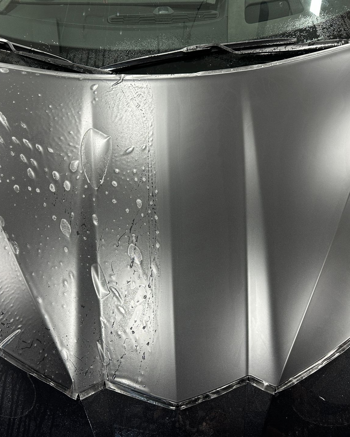 A close-up of a hand pointing to the edge of a piece of paint protection film being applied to a car's black roof panel.