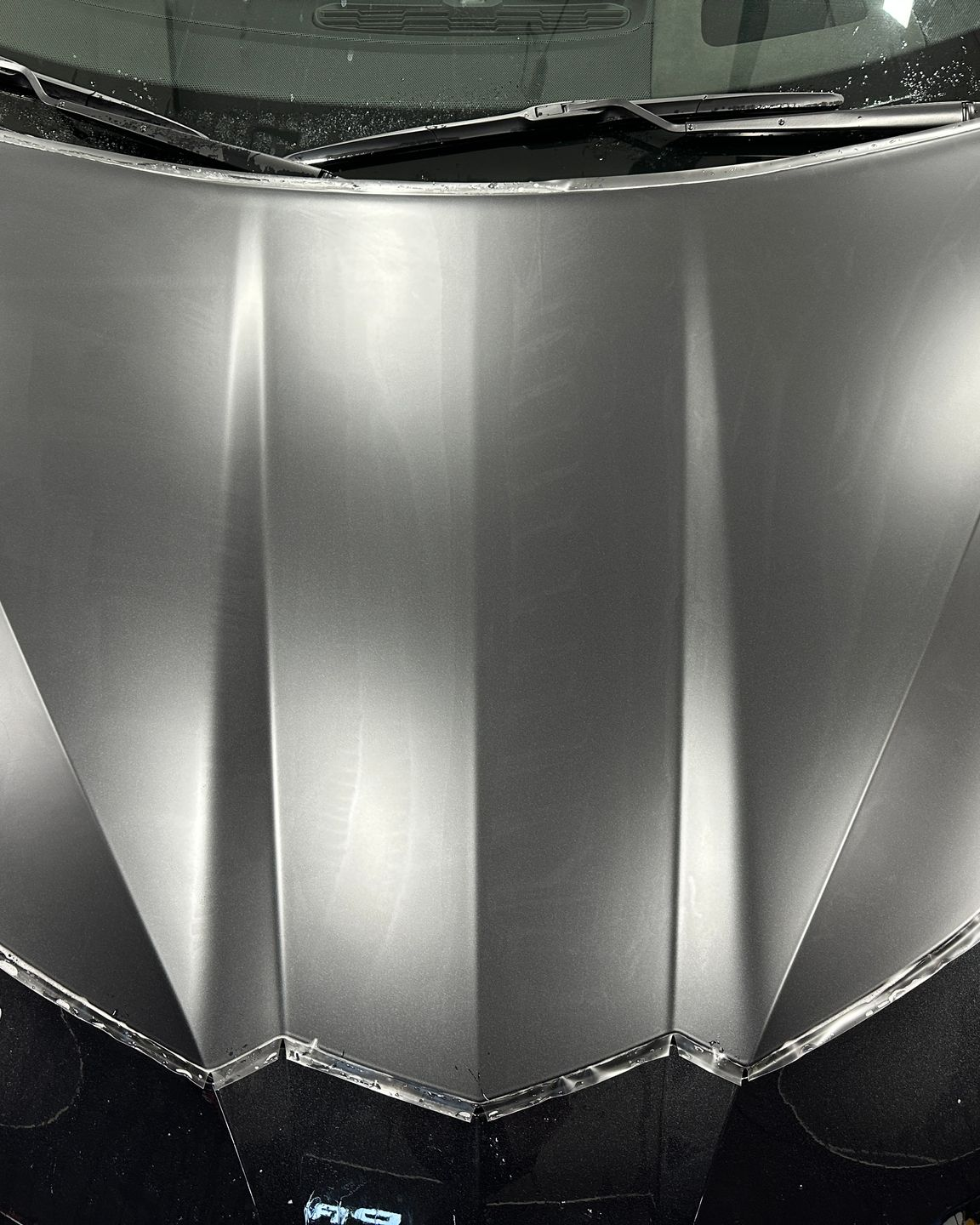 A close-up of a matte black car door edge with a white protective foam strip attached to the side.