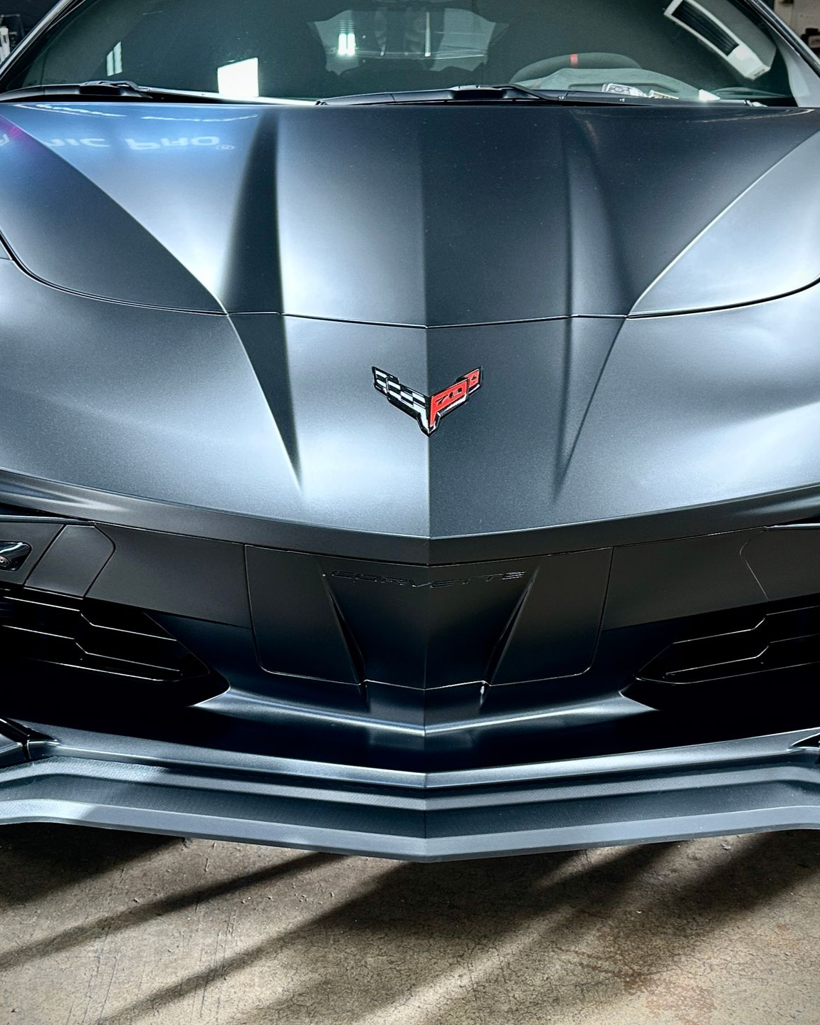 Front view of a matte gray Chevrolet Corvette with red emblem and sharp black grille accents