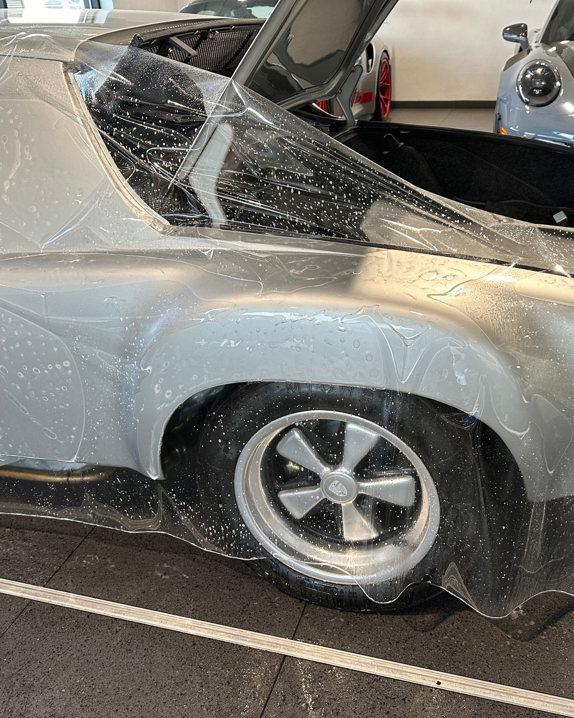 Severely damaged silver classic car with shattered windshield and crumpled rear quarter panel indoors