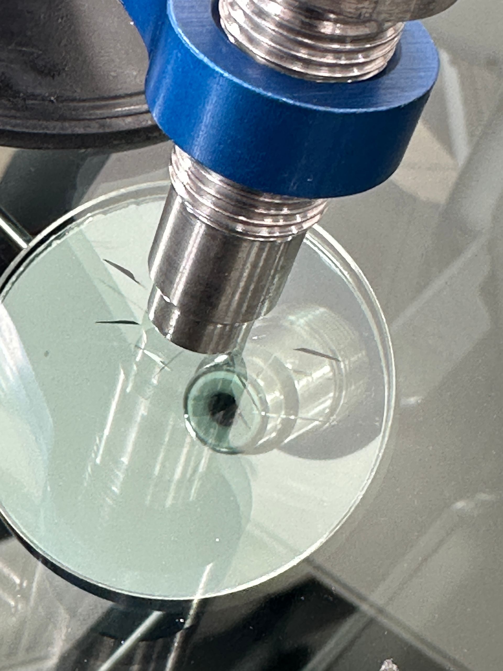 Metal probe inside a clear petri dish on a glass surface, viewed close up.