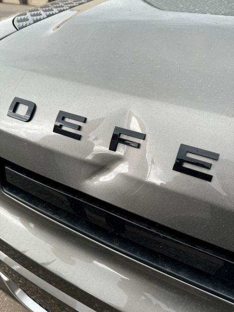 A close-up of a deep dent and paint damage on a black car fender near the orange side marker light.