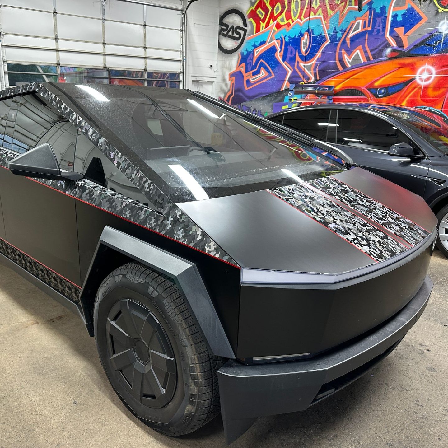 Black Tesla Cybertruck with patterned wrap parked in a graffiti-covered garage