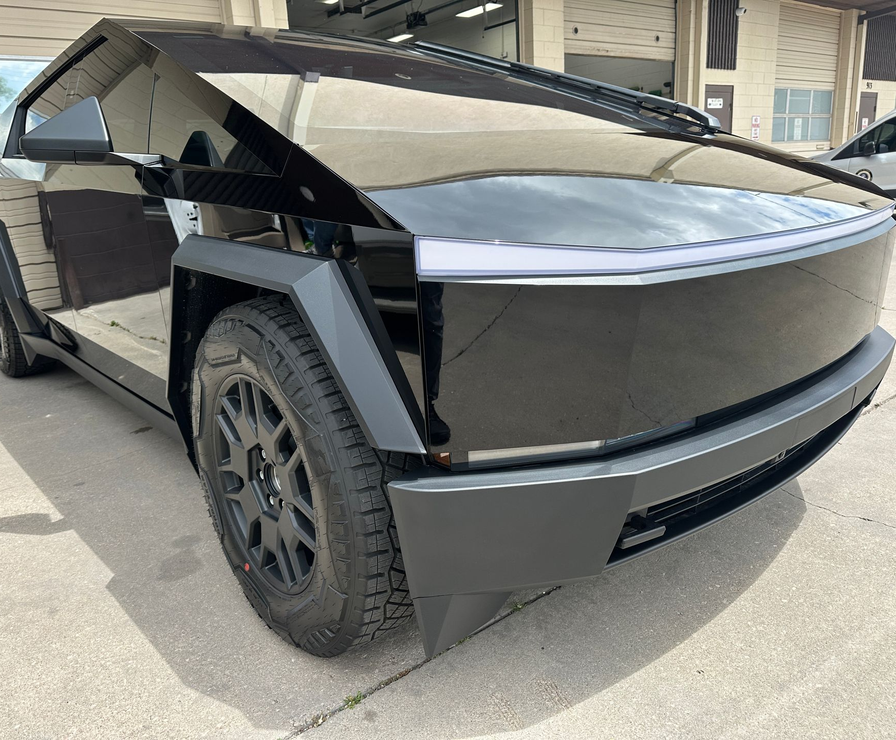 A person in a gray uniform and white glove carefully applies a smooth, metallic copper vinyl wrap to a car body panel.