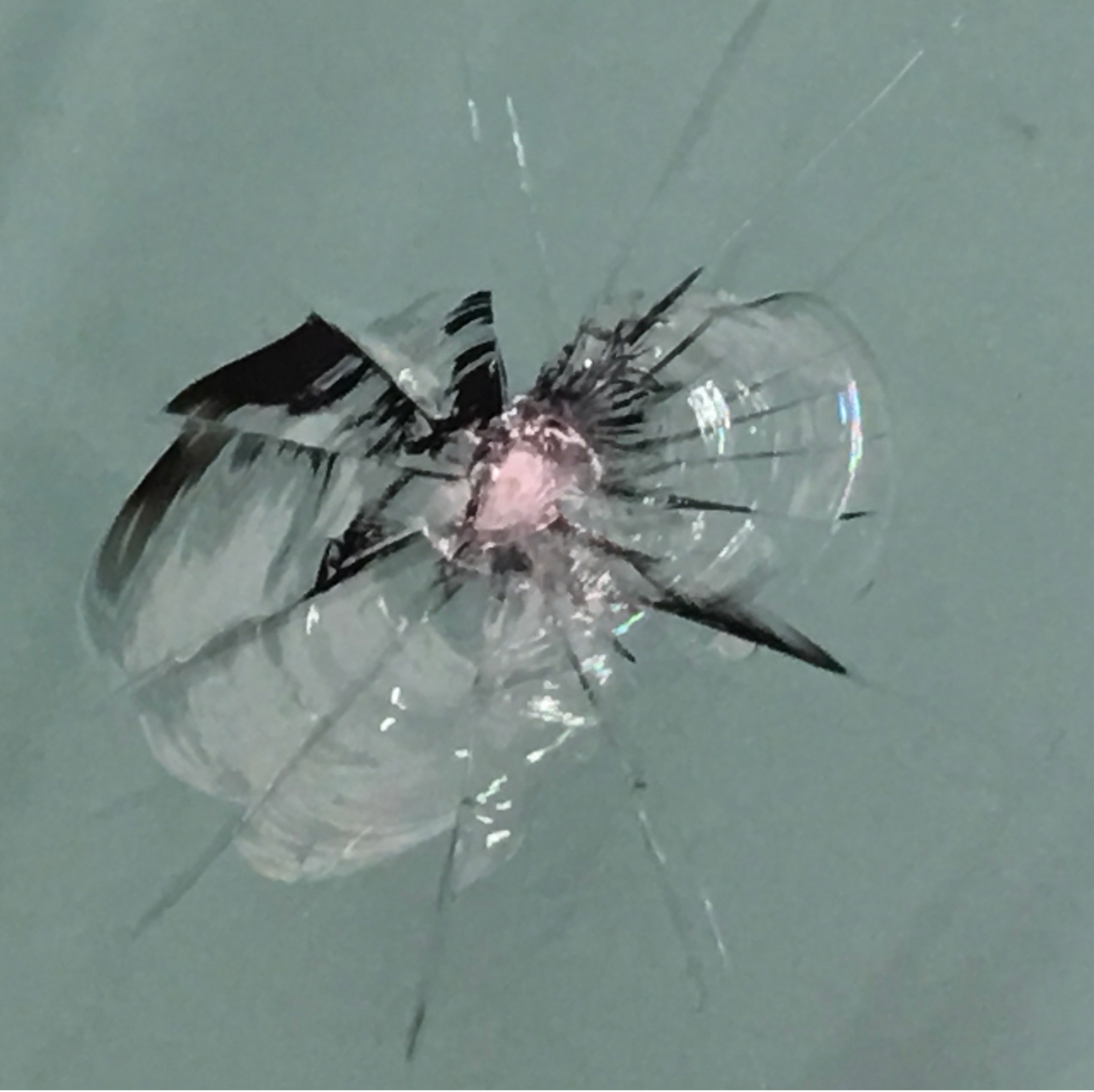 A star-shaped crack with multiple fractures radiating from a central impact point on a glass surface.