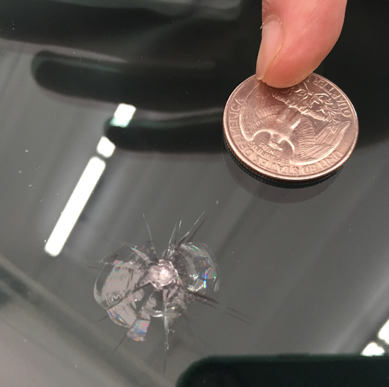 A hand in a purple nitrile glove uses an orange sponge to apply product to a dark, carbon fiber car surface.