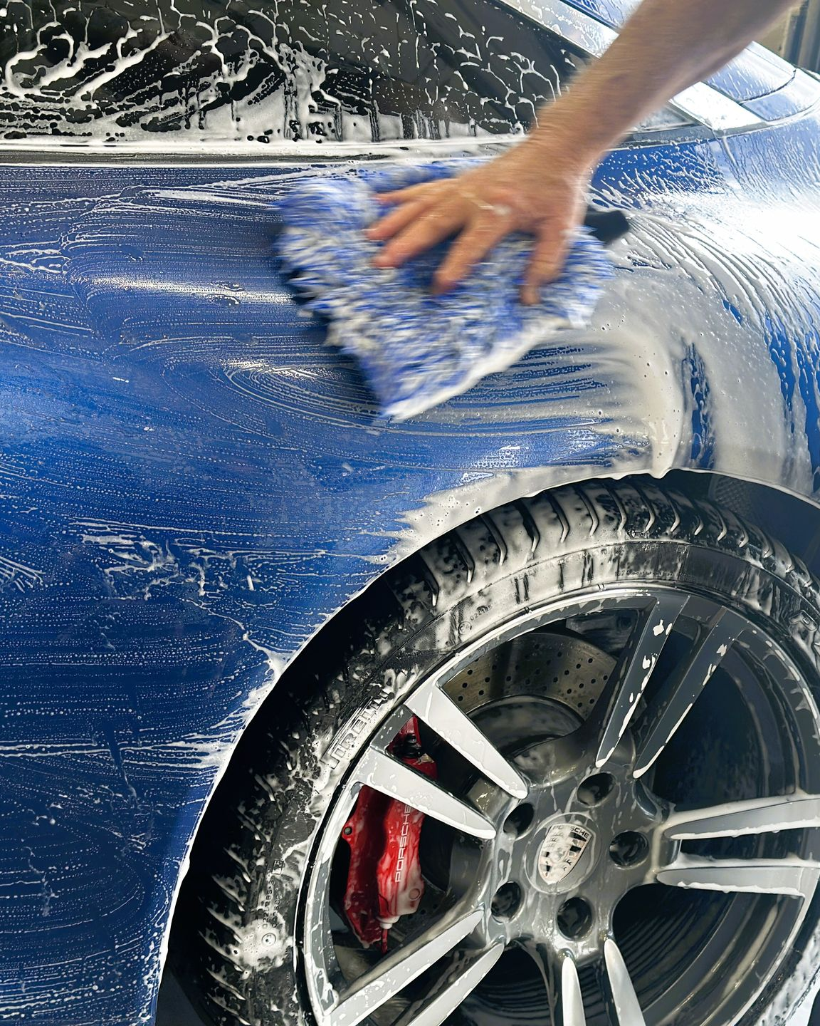 A lime green Lamborghini emblem on a car hood, covered in thick, white soap suds during a wash.