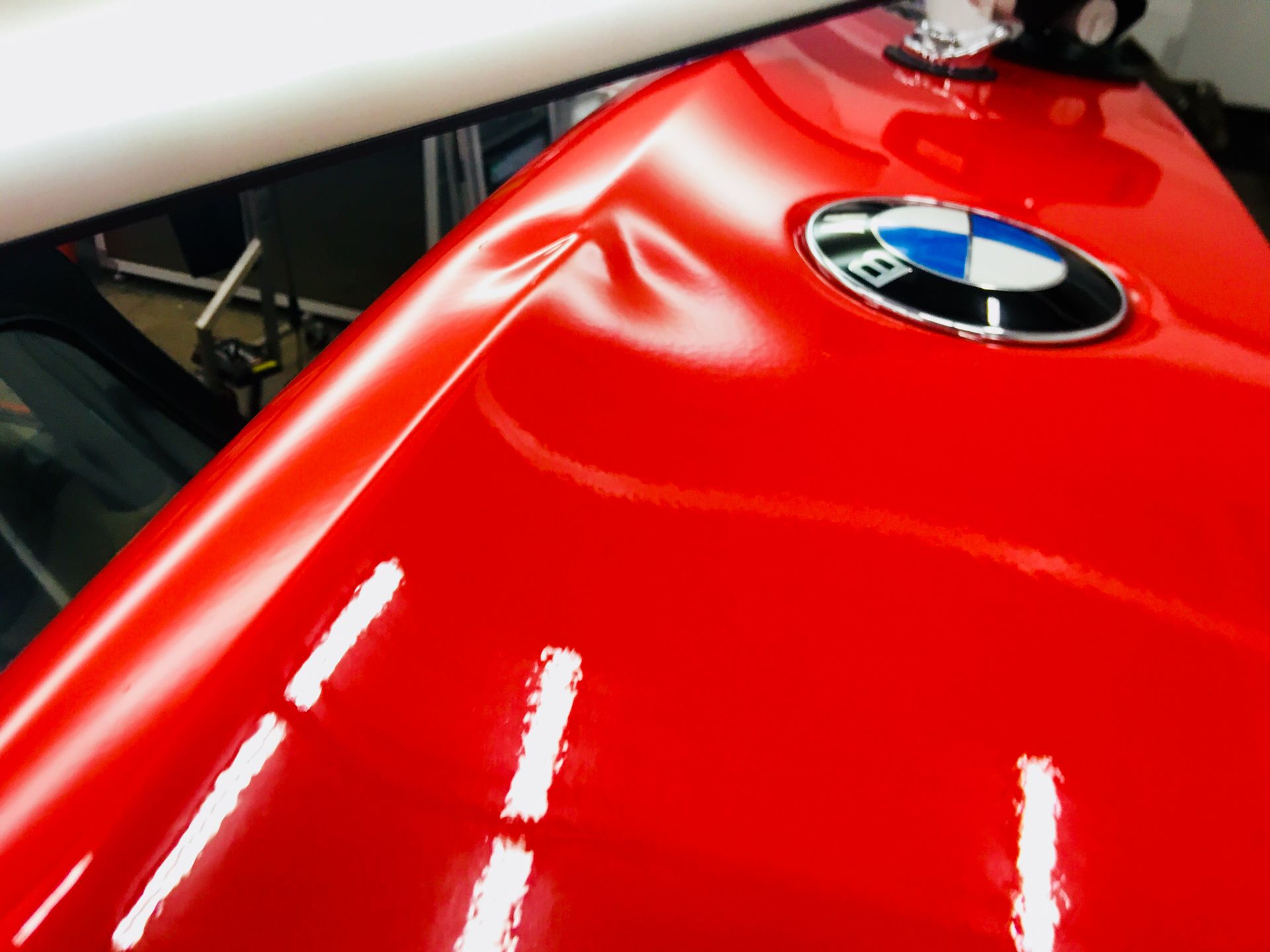Close-up of a glossy red BMW hood with the logo visible indoors
