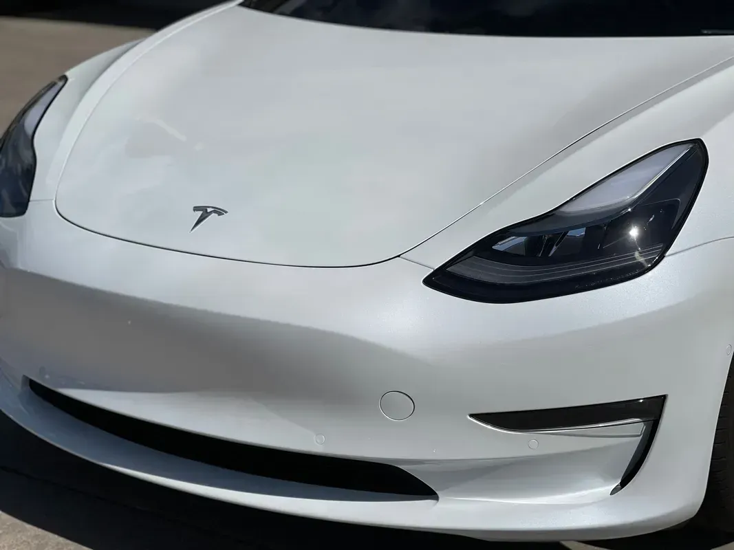 The front view of a white Tesla Model 3, focusing on the hood, LED headlights, and front bumper.