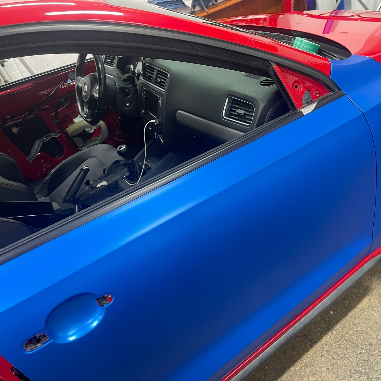 Blue sports car with red interior, viewed through the open driver’s side window.